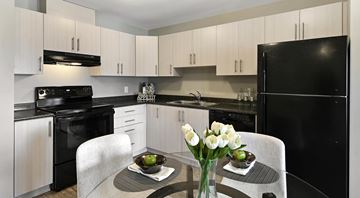 Summerland apartment for rent - A black refrigerator sits in a kitchen with white cabinets and a table with a bowl of fruit and a vase of flowers.
