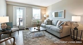 West Kelowna townhouse for rent - A bright open living room with a couch, chairs and coffee table. A single patio door with window next to it and wall mounted AC unit below