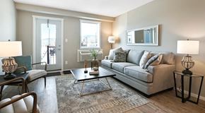 Summerland apartment for rent - A bright open living room with a couch, chairs, coffee table and end tables. Against outer wall a glass patio door, a window with AC unit below