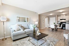 Kelowna apartment for rent - A living room with a grey couch, a coffee table, and a dining area in the background.