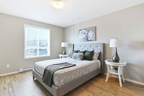 Kelowna apartment for rent - A bedroom with a large bed and a window overlooking a cityscape.