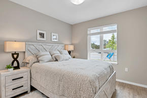 Courtenay apartment for rent - A bedroom with a large bed, two lamps, and a window with a view of trees and a blue flag.