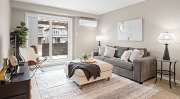 Ottawa apartment for rent - A living room with a grey couch, a white chair, and a table with a lamp on it.