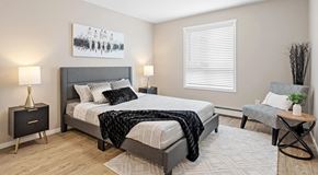 Ottawa apartment for rent - A bedroom with a large bed, a nightstand, a chair, and a painting on the wall.