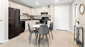 Ottawa apartment for rent - A kitchen with a black fridge, white cabinets, a table with four grey chairs, and a white door.