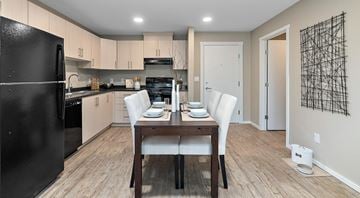 St. Albert apartment for rent - A kitchen with a black refrigerator, wooden dining table with white chairs, and a wall art.