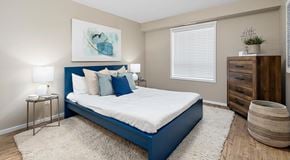 St. Albert apartment for rent - A bedroom with large bed, night stands, a dresser and basket next to a window with blinds