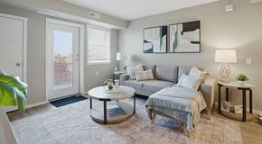Warman apartment for rent - A living room with a small grey sectional, side and coffee table with a window and balcony door