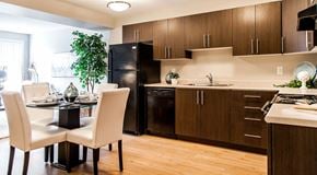 Edmonton apartment for rent - a large open kitchen with dark cabinets, light countertops and black appliances. A round table set for four in the centre of the room