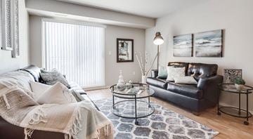 Saskatoon apartment for rent - A living room with a black leather couch, a glass coffee table, and a white sofa with a blanket on it.
