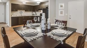Red Deer apartment for rent - An open kitchen with dark cabinets and black appliances with a table set for four