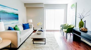 Edmonton apartment for rent - A living room with a white couch, green chairs, and a painting on the wall.