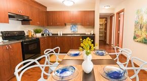 Edmonton apartment for rent - A kitchen with warm wood cabinets, dark counters and black appliances, a long rectangular table runs down the centre of the kitchen