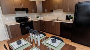 Winnipeg apartment for rent - A warmly lit kitchen with darker wood cabinets, light counter tops and black appliances.