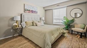 Chestermere apartment for rent - A bedroom with a large bed, a chair, and a window