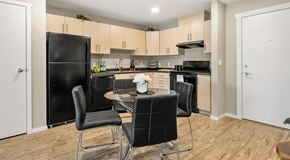 Chestermere apartment for rent - An open concept kitchen with black appliance and light cabinets. A table for four sits in the middle