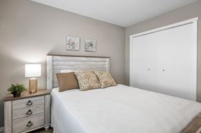 Campbell River apartment for rent - A bedroom with a white bed, a wooden nightstand with a plant and a lamp, and two framed pictures on the wall.
