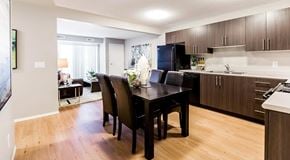 Beaumont townhouse for rent - An apartment kitchen with dark cabinets and light counter tops, black appliances and a table set for four
