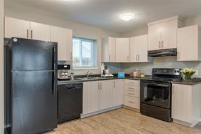 Campbell River apartment for rent - A black refrigerator is in a kitchen with wooden floors and cabinets.