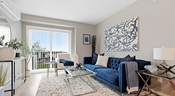 Portage La Prairie apartment for rent - A blue couch sits in a living room with a glass table and a large abstract painting on the wall.
