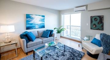 Winnipeg apartment for rent - A living room with a grey couch, a glass table, and a painting on the wall.