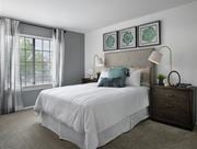 Rochester Hills townhouse for rent - Bright bedroom at River Oaks at Rochester Hills Apartments with white bed linens, two nightstands, lamps, and window blinds.