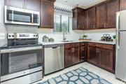 Rochester Hills townhouse for rent - Kitchen with stainless appliances, dark wood cabinets, white backsplash, patterned rug at River Oaks in Rochester Hills.