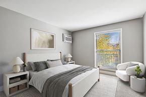 Aurora apartment for rent - A bedroom with a large bed, a nightstand with a lamp, a chair, and a window with a view of trees outside.
