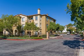 San Diego apartment for rent - A large beige building with a red fence and gate in front.