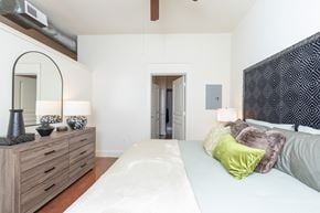Houston apartment for rent - A bedroom with a white bed and a wooden dresser with a mirror.