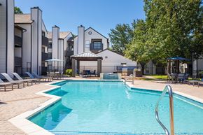 Houston apartment for rent - A swimming pool surrounded by lounge chairs and umbrellas in front of a building.