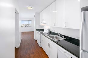 San Francisco apartment for rent - Two-BR Apartments in San Francisco, CA - Trinity Place at 1190 - Kitchen with White Cabinets, Black Granite Countertops, White Appliances, Wood-Style Flooring, and a Window