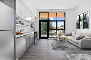 Los Angeles apartment for rent - A modern kitchen with a refrigerator on the left and a living room with a couch and a coffee table on the right.