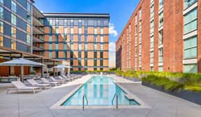 Charleston apartment for rent - A swimming pool surrounded by lounge chairs and umbrellas in front of a modern building.