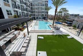 Houston apartment for rent - A large swimming pool is surrounded by a grassy area and palm trees.
