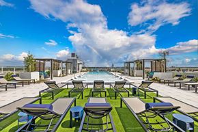 Tampa apartment for rent - a rooftop pool with lounge chairs and tables and a rainbow in the sky