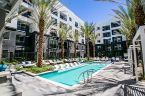 Las Vegas apartment for rent - an outdoor swimming pool with chaise lounge chairs and palm trees in front of an apartment building