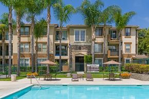 Chula Vista apartment for rent - A swimming pool is surrounded by lounge chairs and umbrellas in front of a large apartment building.