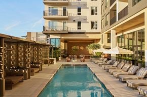 San Diego apartment for rent - A large swimming pool surrounded by lounge chairs and umbrellas in front of a modern building.