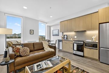 Portland apartment for rent - A modern living room with a brown leather couch and a kitchen area with stainless steel appliances.