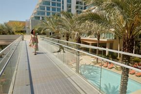 San Marcos apartment for rent - A woman in a dress walks on a bridge with palm trees and a pool in the background.