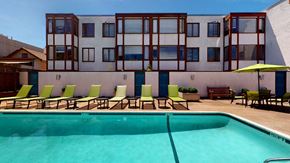 San Francisco apartment for rent - a swimming pool with green lounge chairs and yellow umbrellas in front of a white building