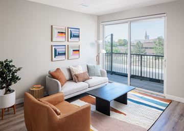 Denver apartment for rent - A living room with a grey couch, a brown chair, a coffee table and a plant.