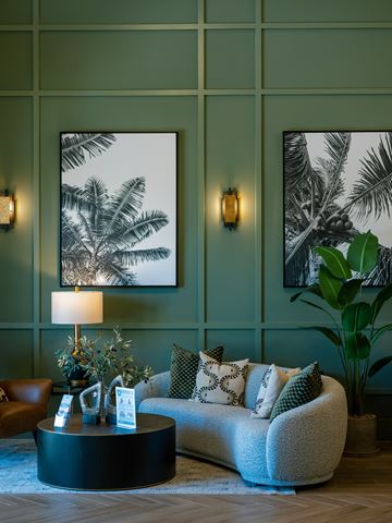 Orlando apartment for rent - A living room with a grey couch, a round table with a lamp and a plant on it, and two framed pictures on the wall.