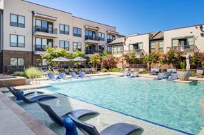 Flower Mound apartment for rent - A swimming pool surrounded by lounge chairs and umbrellas in front of apartment buildings.