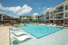 Flower Mound apartment for rent - A large swimming pool surrounded by white lounge chairs and umbrellas.