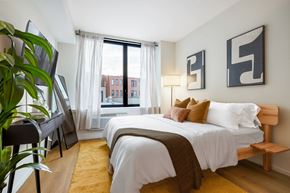 Jersey City apartment for rent - A bedroom with a large bed and a view of a cityscape through the window.