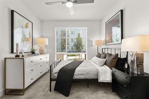 Sacramento apartment for rent - Studios in Sacramento, CA - The Eisley - Bedroom with Plush Carpeting, Ceiling Fan, a Large Bed with Black Nightstand, and Oversized Window