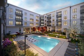 Charlotte apartment for rent - A swimming pool is surrounded by lounge chairs and trees in front of apartment buildings.
