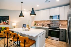 Las Vegas apartment for rent - a kitchen with white cabinets and a large white island with a white countertop and orange chairs